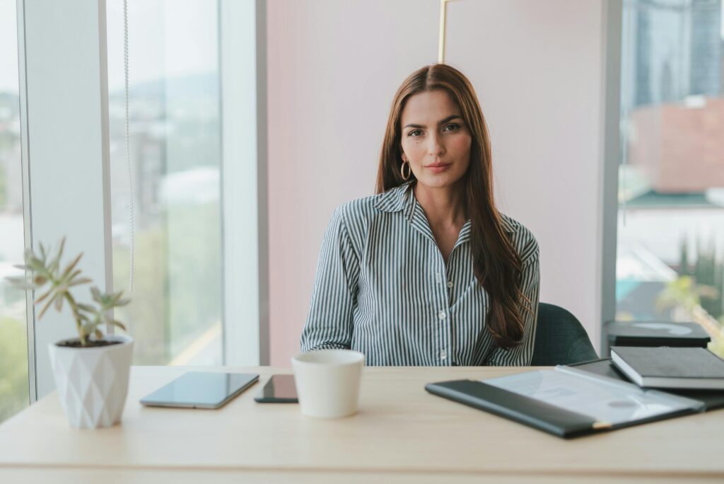 pexels-photo-10041270-10041270 Portrait of a businesswoman with brown hair sitting at a desk in a modern office environment.