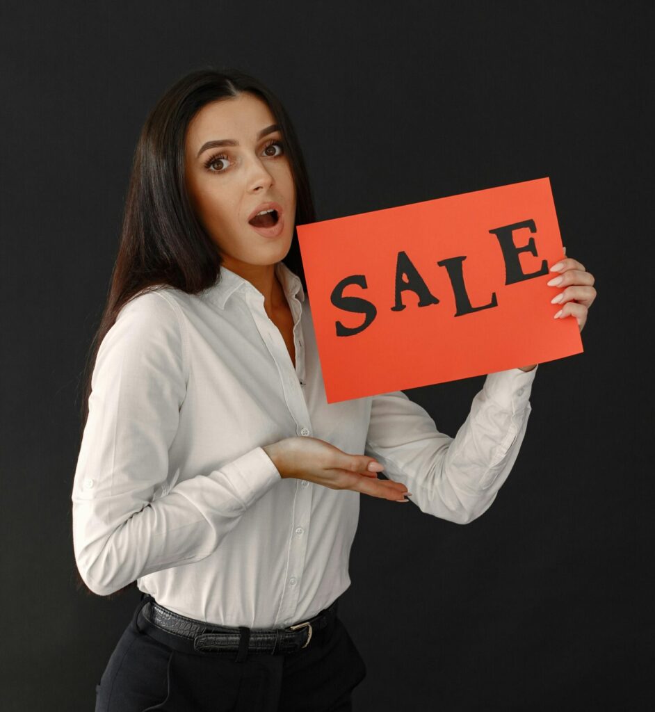 Surprised woman holding a sale sign against a black background in a studio setting.